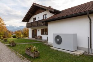 Einfamilienhaus in Oberbayern mit Holzbalkon und Außeneinheit einer Luft-Wasser-Wärmepumpe, im Hintergrund die Alpen