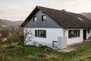 Weiß verputztes Einfamilienhaus mit verschiefertem Giebel in Osthessen, daneben eine Luft-Wasser-Wärmepumpe